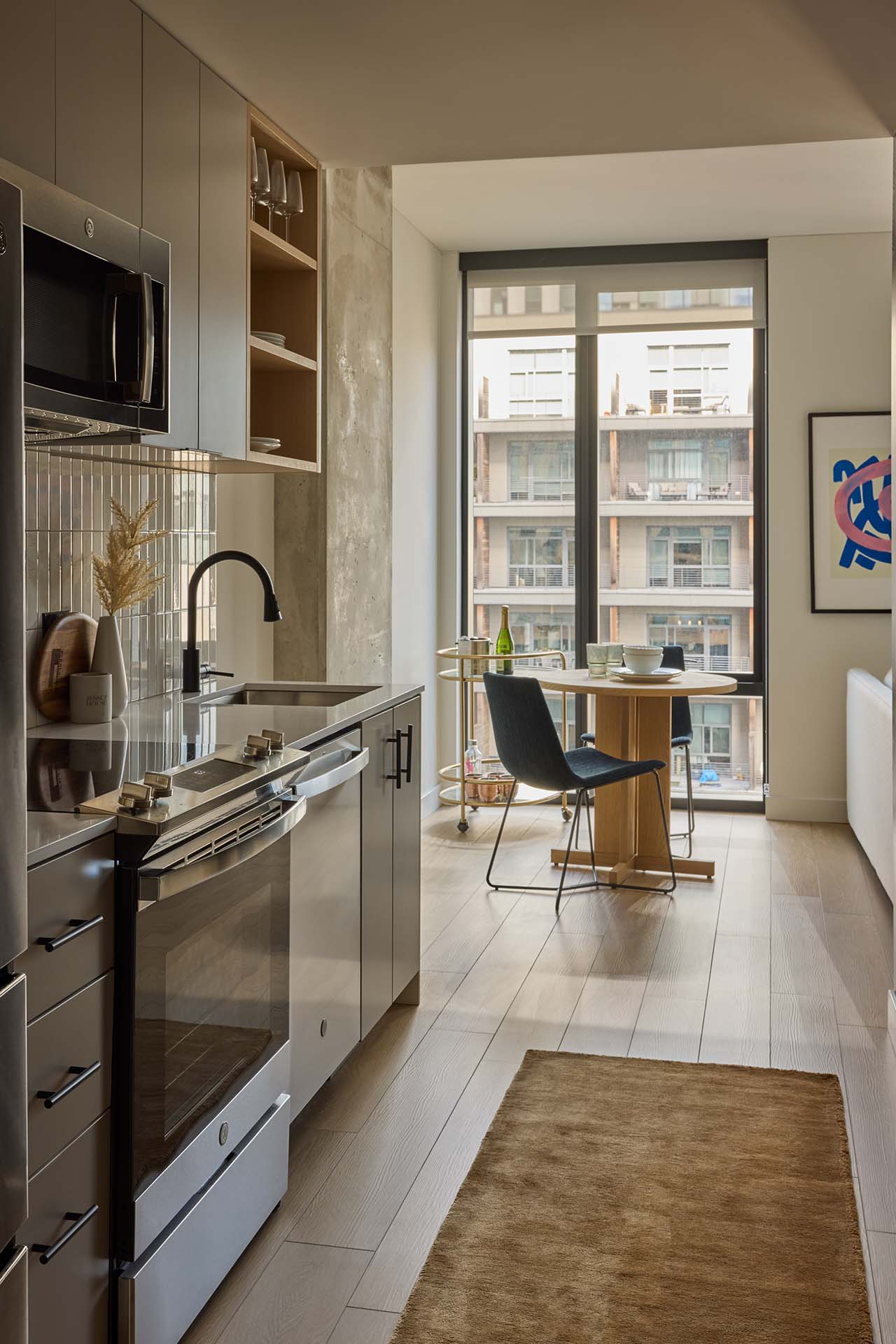 Gallery kitchen with stainless steel appliances and stylish backsplash. Luxury plank flooring and room for dining area in front of the floor-to-ceiling window.