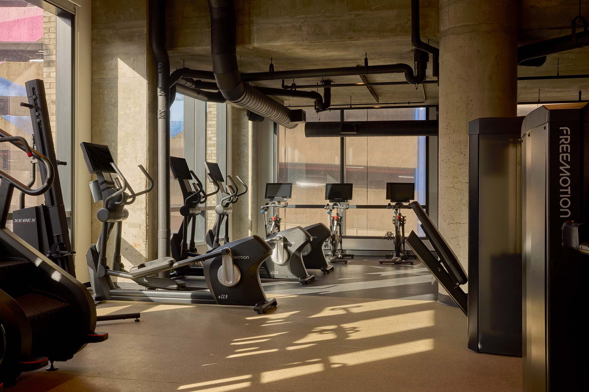 Jessup House community fitness center with cardio machines and large windows.